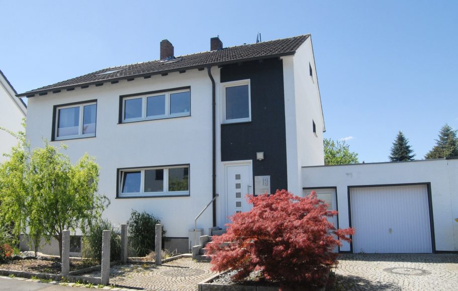 Hausansicht Modernes zweigeschossiges Wohnhaus mit Garage und roten Sträuchern im Vorgarten.