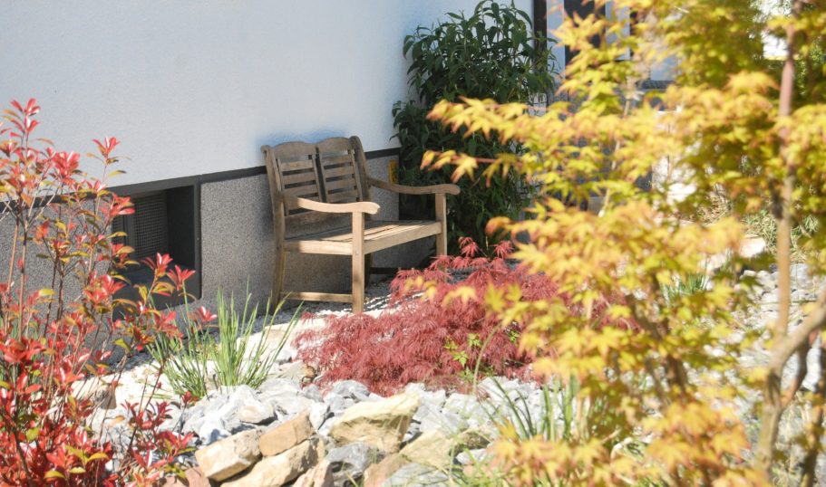 Vorgarten Holzbank in einem Garten mit bunten Pflanzen und Steinen.